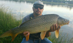 Mike Medina proudly holds a 21 pound common carp along the shores of a tranquil lake.