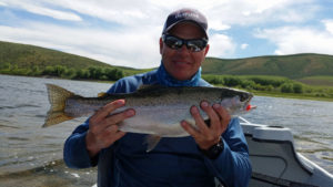 Chris Galvin holding a large rainbow trout caught fly fishing from a drift boat loch style