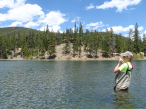 Boy holding bent fly fishing rod wading in a trout lake with scenic mountain view
