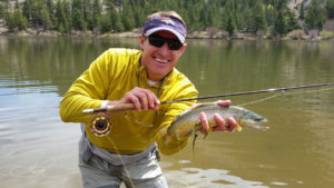 Fly fishing angler holds a brown trout with one hand and fly rod with the other