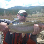 Fly fishing angler holding enormous rainbow trout while holding fly rod in mouth