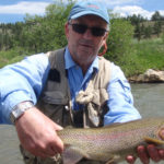 Angler holding a large rainbow trout with sunny mountains behind