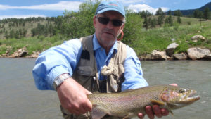 Angler holding a large rainbow trout with sunny mountains behind