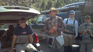 Several anglers in waders standing by their fishing vehicles