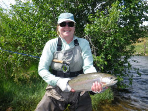 Woman poses with Colorado rainbow trout with fly rod tucked away under her arm