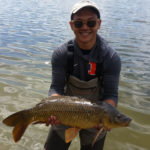 Young angler proudly holding a big carp with lake behind him