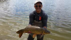 Young angler proudly holding a big carp with lake behind him