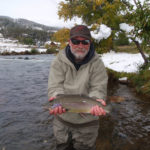 A pretty rainbow trout held above the river with a coating of early snow in the background.
