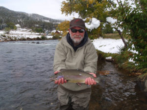 A pretty rainbow trout held above the river with a coating of early snow in the background.
